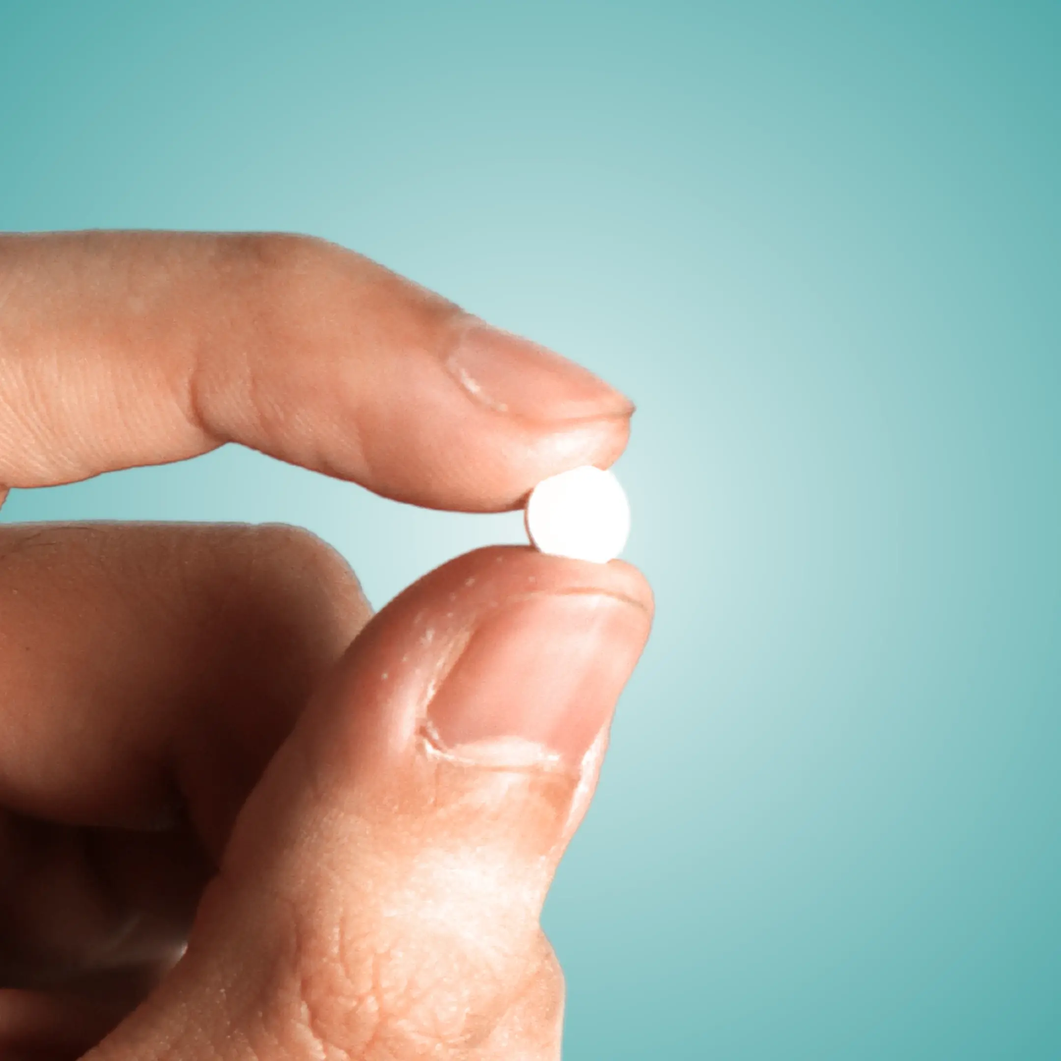 two fingers holding a finasteride tablet